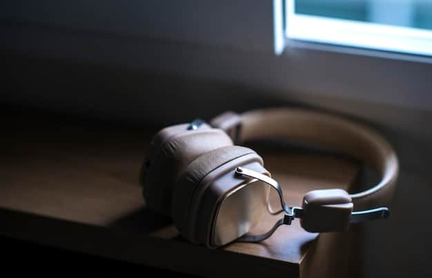 Close-up shot of a pair of over-ear noise-cancelling headphones resting on a desk in a brightly lit office. The focus is on the headphone's design and the office environment in the background.