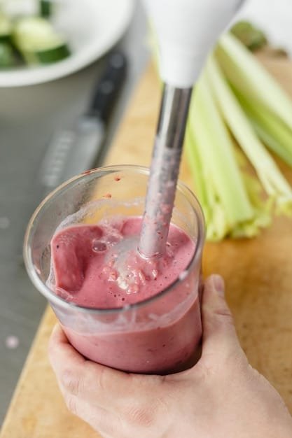 A vibrant smoothie being poured from a high-powered blender into a glass. The blender is sleek and modern, with a clear container showcasing the blended ingredients.