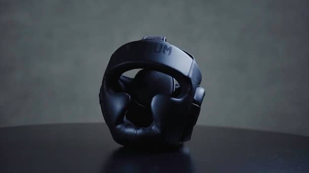 A close-up shot of a high-quality gaming headset with vibrant RGB lighting. The headset is placed on a stand, and the background is a blurred gaming setup with multiple screens.
