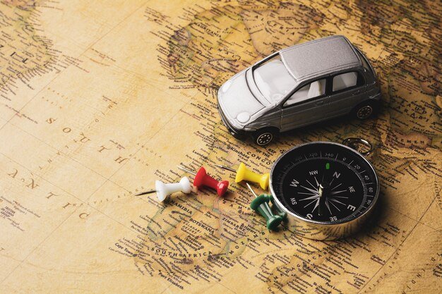 An open road map with highlighted routes and points of interest marked with pins. A compass and a set of car keys are placed on the map.